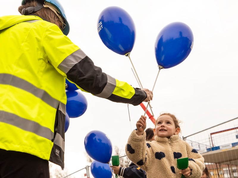 En liten flicka håller upp blå ballonger i luften.