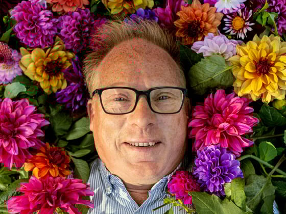 En man med glasögon är omgiven av blommor.