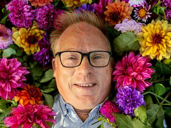 En man med glasögon är omgiven av blommor.