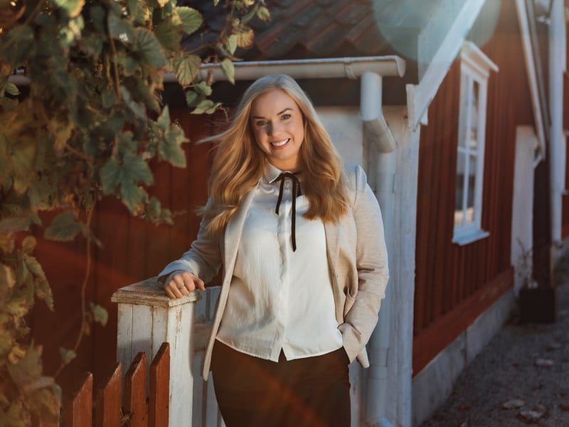 En kvinna står på en veranda bredvid ett hus.