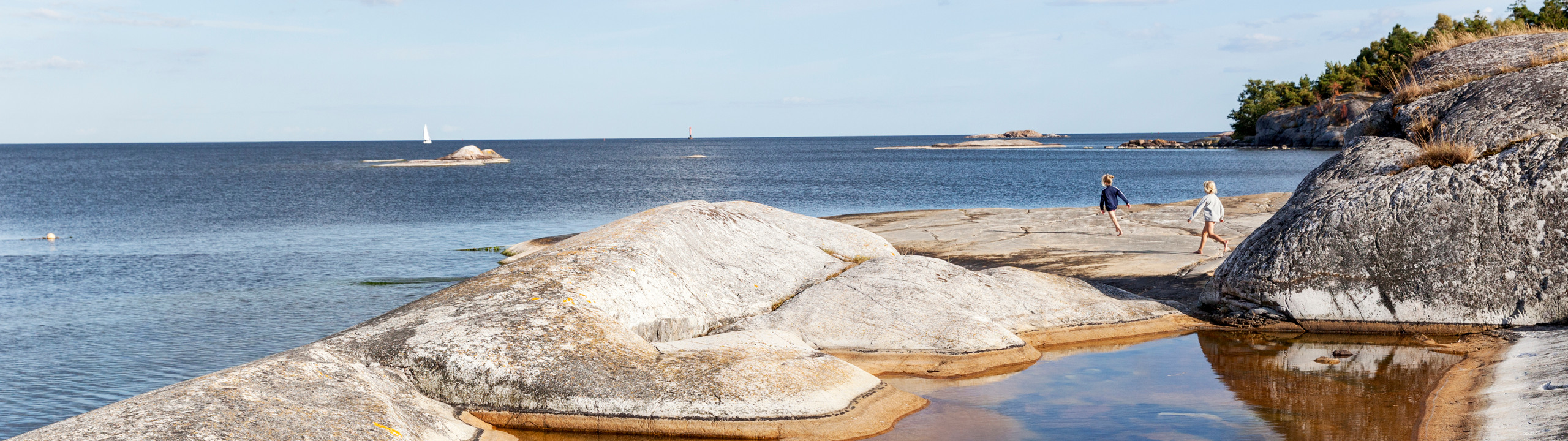 Två barn springer på klippor vid havet.