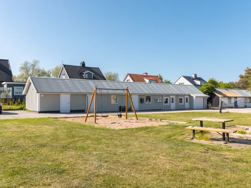 En park med en lekplats och ett hus i bakgrunden.