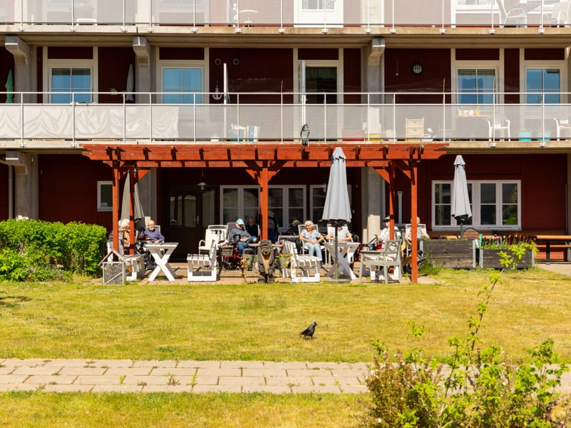 En grupp människor som sitter på solstolar framför en byggnad.